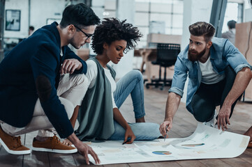 Canvas Print - Group of confident business people discussing strategy while looking through a blueprint together