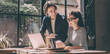 © gstockstudio - Two confident young people looking at laptop and smiling while working in the office together