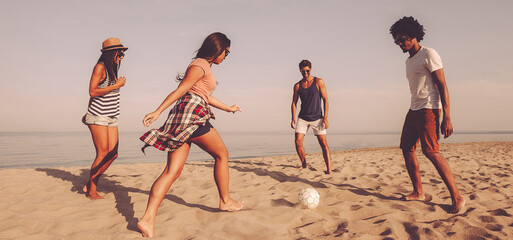 Wall Mural - Group of cheerful young people playing with soccer ball on the beach