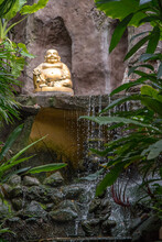Golden Buddha Statue In The Tropical Garden With Waterfall