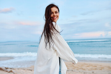 Wall Mural - Brunette woman with long hair in a white shirt and jean shorts tan and happy running on the beach and having fun smile with teeth in front of the ocean, vacation summer trip