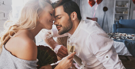 Poster - Young loving couple holding champagne flutes while sitting face to face indoor