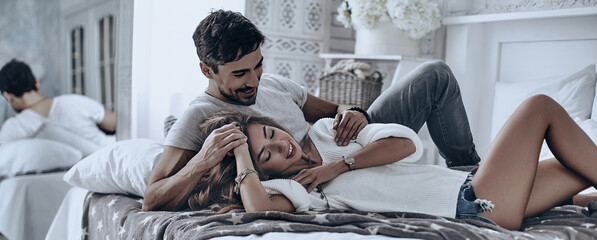 Wall Mural - Beautiful young couple lying on the bed and smiling while spending time at home together