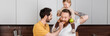 © LIGHTFIELD STUDIOS - Gay man feeding husband near smiling daughter with green apple in kitchen, banner.
