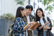 © crizzystudio - Group of happy young Asian students in casual clothes sitting on the front steps of a university building looking for educational information. teamwork classmate best friend.