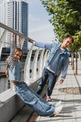 Wall Mural - full length of stylish kids in denim vests and jeans posing near metallic fence on riverside.