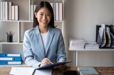Poster - Businesswoman working on her project while sitting in the office room, holding chart and graph paper in her hands.