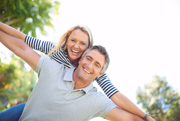 Wall Mural - Playful partners. Cropped portrait of a handsome mature man piggybacking his wife in the park.