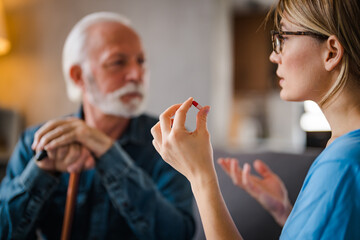 Wall Mural - Senior male patient consult with physician nurse at nursing home. Caregiver therapist pharmacist girl hold medicine pills bottle, explain prescription to elderly old man in living room in house.