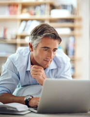 Poster - Feeling a little reflective. a handsome mature man lying on his living room floor using a laptop.