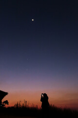 Women taking picture of nature observing evening sky with stars, planets and crescent moon. Moon meets Jupiter and Venus in the twilight sky.