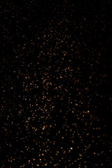 natural organic dust golden particles floating on a sunbeam on black background. glittering sparklin