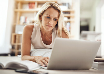 Poster - Working on her blog. a beautiful mature woman lying on her living room floor using a laptop.