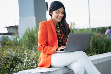 Confident smiling Indian woman, copywriter using laptop typing working freelance project online sitting at workplace. Successful asian student studying, learning in university campus. Online education