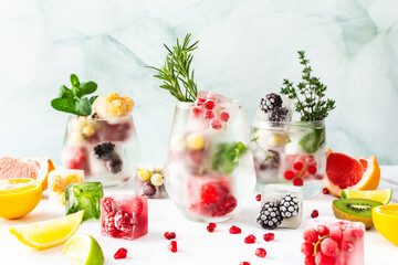 Refreshing drinks with ice cubes with fruits and citrus fruits, ice with blackberries and raspberries, gooseberries and currants, with mint, a jug of water and citrus fruits