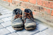 Dirty old shoes on paveng floor. A pair of dirty boots. Old worn leather shoes with variegated brown laces. The concept of poverty, homelessness, lack of money. Selective focus