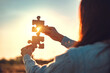 © oatawa - Closeup hands of woman connecting jigsaw puzzle with sunlight effect, Jigsaw alone wooden puzzle against sunset, Business partner, Success and strategy concept