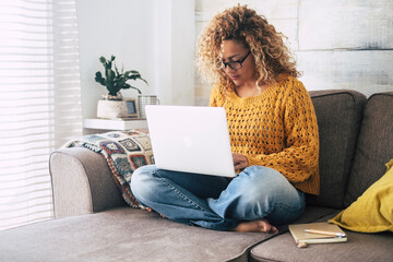 One adult modern woman at home working on laptop alone sitting on the sofa inside apartment, Indoor technology leisure activity female people surfing the net on notebook computer. Smart working relax