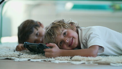 Canvas Print - Portrait of joyful child holding tablet device lying on floor turning head to camera smiling. Kids close up face posing