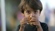 © Marco - Portrait of child eating piece of bread croissant. Close up face of one small boy kid eating carb food
