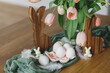 Beautiful tulips, eggs and bunny decoration on wooden table. Modern farmhouse easter decor. Happy Easter! Stylish handmade egg holder, natural eggs, pink tulips bouquet and rustic bunnies