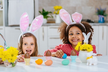 Two girls with Bunny ears on her heads is happy find a chokolate eggs after Easter egg hunt.