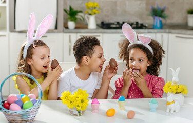 three children in bright clothes eating easter eggs