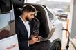 © sofiko14 - Focused man in business suit drinking coffee and working on laptop while charging battery of modern electro car. Concept of people, transport and technology.