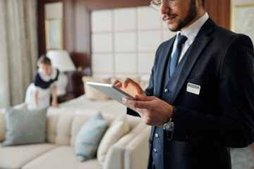 Aufkleber - Young elegant manager of luxurious hotel using tablet against chambermaid changing bedclothes and preparing room for new guests
