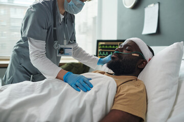Poster - Cropped shot of nurse in mask and gloves taking care of sleeping patient with oxygen cannula in nose and bandage around head