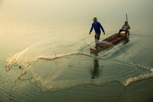 Fisherman On Boat Throwing Fishing Net In Morning Sunshine At Lake. Asian Fisherman Thailand