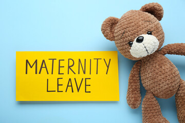 Wall Mural - Toy bear and note with words Maternity Leave on light blue background, flat lay