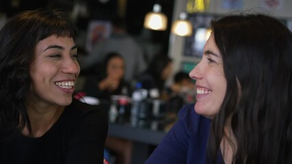 Wall Mural - Happy female friends laughing and smiling at cafe restaurant while in conversation and gossip