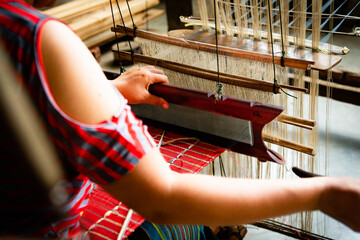 horizontal photo from behind of the hands of a silk weaver working on her loom on a red piece of tex