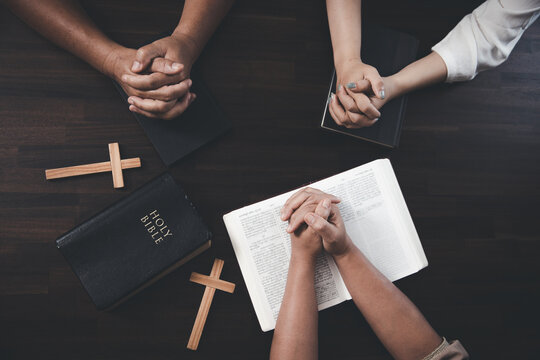 Small groups of Christians hold hands and pray together around a wooden table with bible pages and crosses. bible study group Learning religious concepts in the Bible. Worship God.