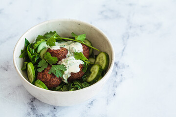 Canvas Print - Green salad with falafel, tahini dressing in white bowl on white marble background. Alternative vegan recipe.