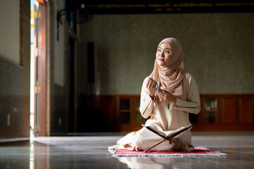 The image of an Asian Muslim woman in the Islamic religion in hijab in cream color. Sitting reading the Quran and having a happy smiling face Staying in a beautiful mosque out of respect for God.