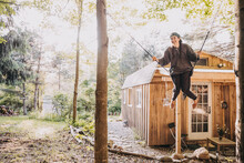 Young Woman Swings Outside Of A Rustic Camp Cabin In The Woods In NY