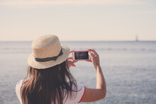 Young Travelling Woman In Hat Taking Photos Of Summer Sunny Sea