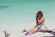 © Cavan Images - Western girl in bikini taking photo on a pristine beach in Cuba