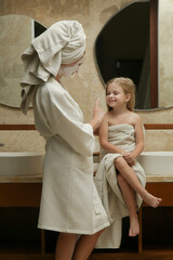 Portrait of mother with her little daughter wrapped in towels in the bathroom having fun during skin care routine and good family time together