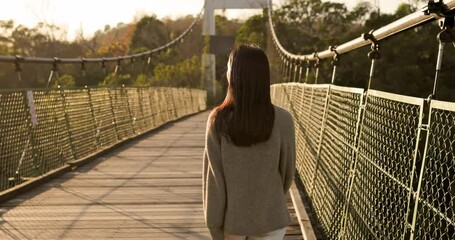 Poster - Woman walk along the wooden suspension bridge at sunset time