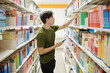 © DragonImages - College student with smartphone taking book from shelf