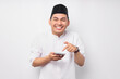 © Bangun Stock Photo - Excited young Asian Muslim man wearing Arabic clothes pointing finger at smartphone isolated on white background. People religious Islamic lifestyle concept