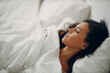 © primipil - Beautiful brunette young woman covering white blanket sleep in bed at bedroom.