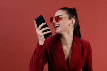 Sticker - Young laughing woman in red glasses and suit listening portable wireless speaker. Listen bluetooth music and dancing.