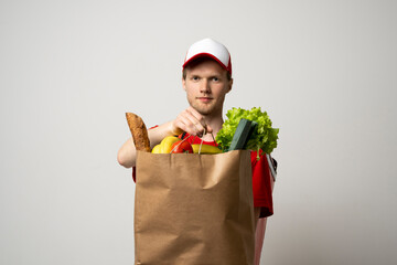 Wall Mural - Delivery man employee in red cap and t-shirt uniform hold craft paper packet with food isolated on white background studio.