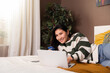 © ABCreative - Photo of delighted asian kazachstan girl in casual clothes outfit smiling at camera while laying on bed in front of laptop computer doing purchase shopping online holdin credit card in hands.
