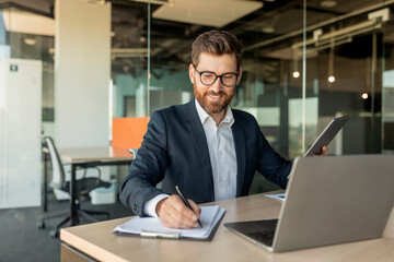 Man CEO or manager filling out paperwork in his office, sitting in front of laptop, signing contract