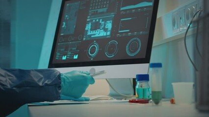 Unrecognizable scientist in gloves and coverall doing research in laboratory, working with biochemical material in test tubes sitting by computer at work desk